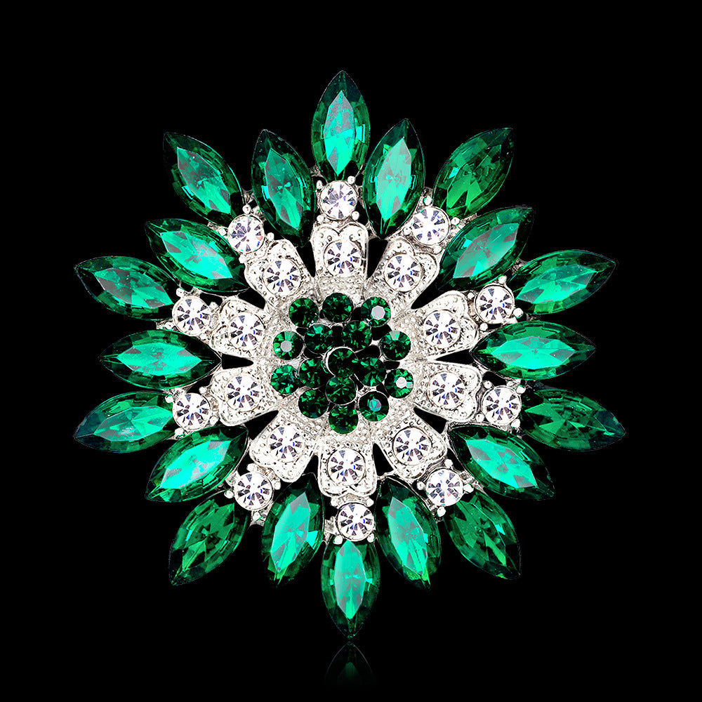 Decorative brooch with green and clear gemstones on a black background