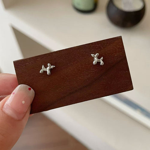 Silver dog-shaped earrings on a wooden display card held by a hand.