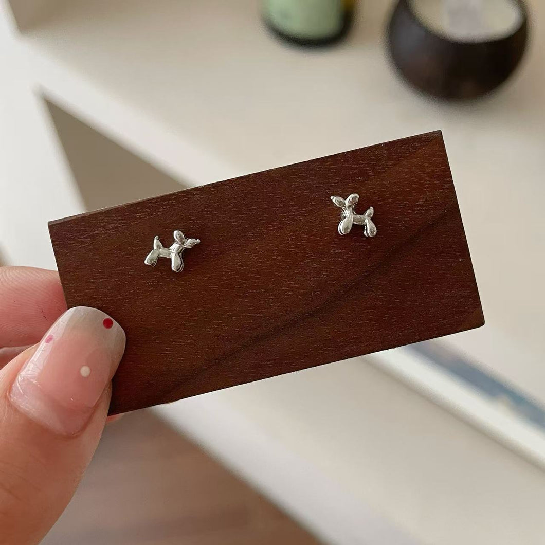 Silver dog-shaped earrings on a wooden display card held by a hand.