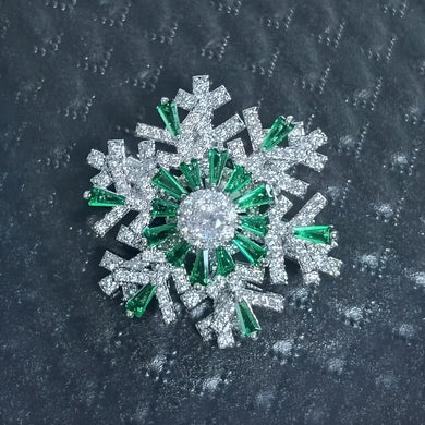 Snowflake-shaped brooch with green and clear gemstones on a dark textured background