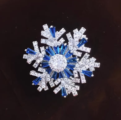 Decorative snowflake brooch with blue and clear gemstones on a dark background