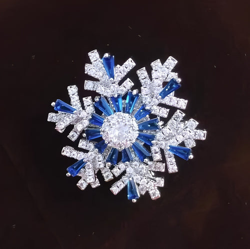 Decorative snowflake brooch with blue and clear gemstones on a dark background