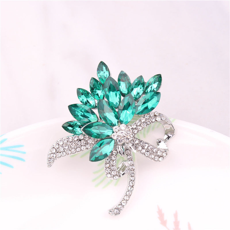 Teal gemstone brooch with silver bow on a white background