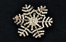 Load image into Gallery viewer, Gold snowflake-shaped brooch on a black background