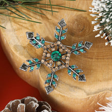 Load image into Gallery viewer, Decorative snowflake brooch with gemstones on a wooden surface with Christmas decorations.