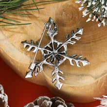 Load image into Gallery viewer, Silver snowflake ornament on a wooden surface with pine branches and pinecones.