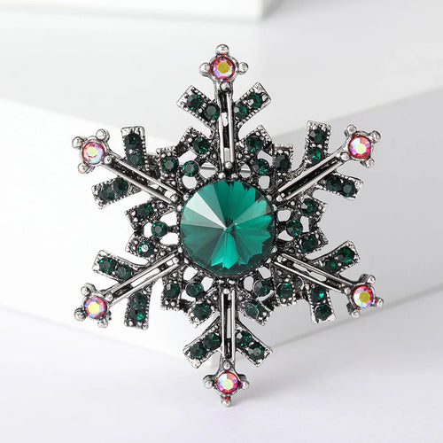 Snowflake-shaped brooch with green gemstone and multicolored accents on a white background