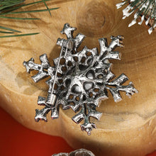 Load image into Gallery viewer, Silver snowflake ornament on a wooden surface with greenery